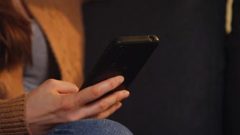 Close-Up-On-Hand-Of-Woman-Sitting-On-Sofa-At-Home-Using-Mobile-Phone-To-Check-Social-Media-Message-And-Scrolling-Online